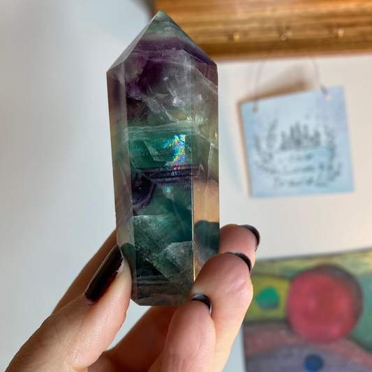 A rainbow fluorite tower is held by a woman's hand.