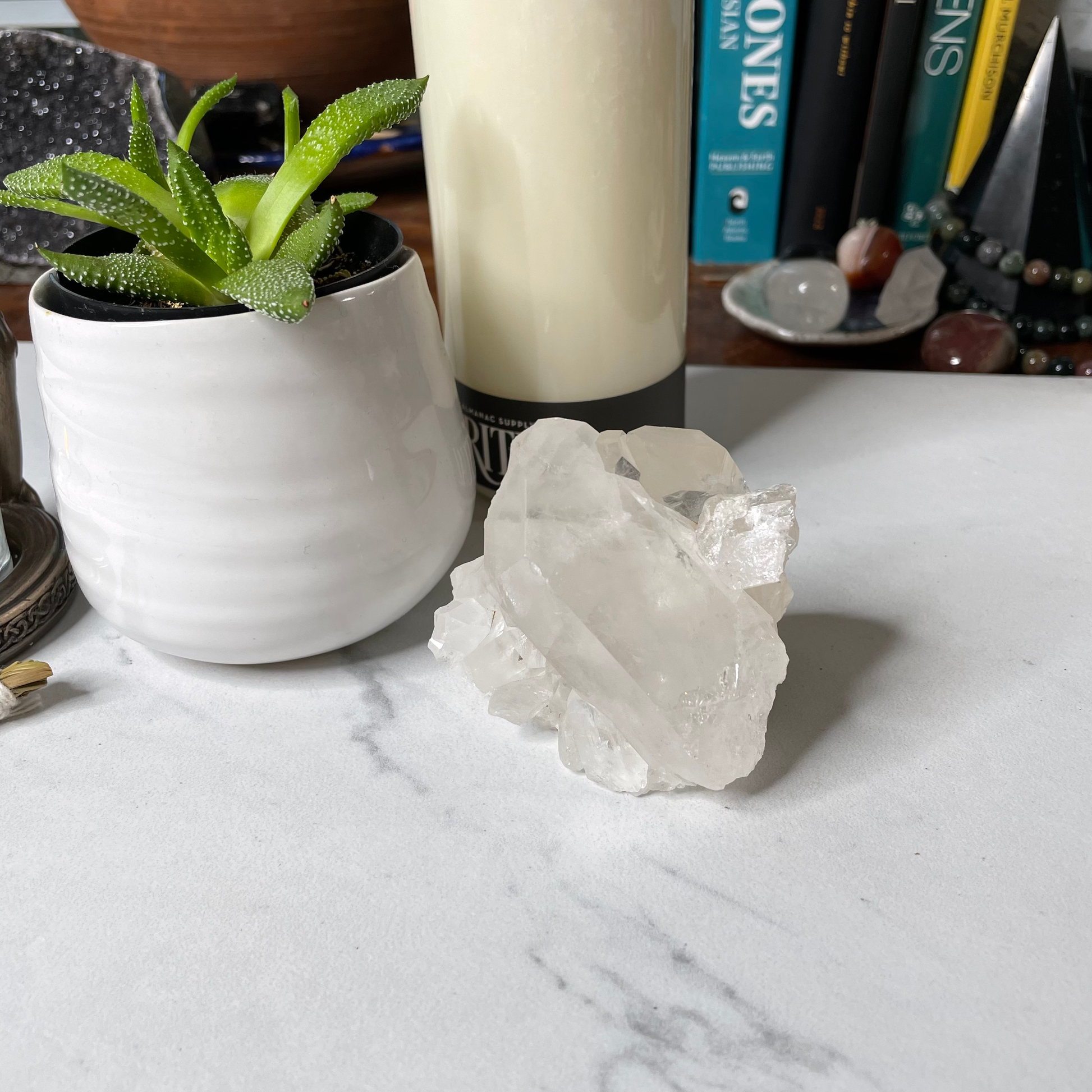 Freya's Haven | Metaphysical & Crystal shop | A close up photo of a Clear Quartz Cluster displayed on a white marble tile with candles in the background.