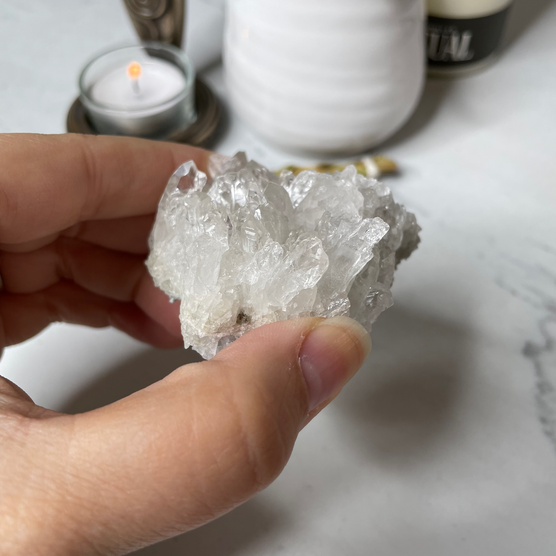Freya's Haven | Metaphysical & Crystal shop | A close up photo of a Clear Quartz Cluster held in a woman's hand with candles in the background.