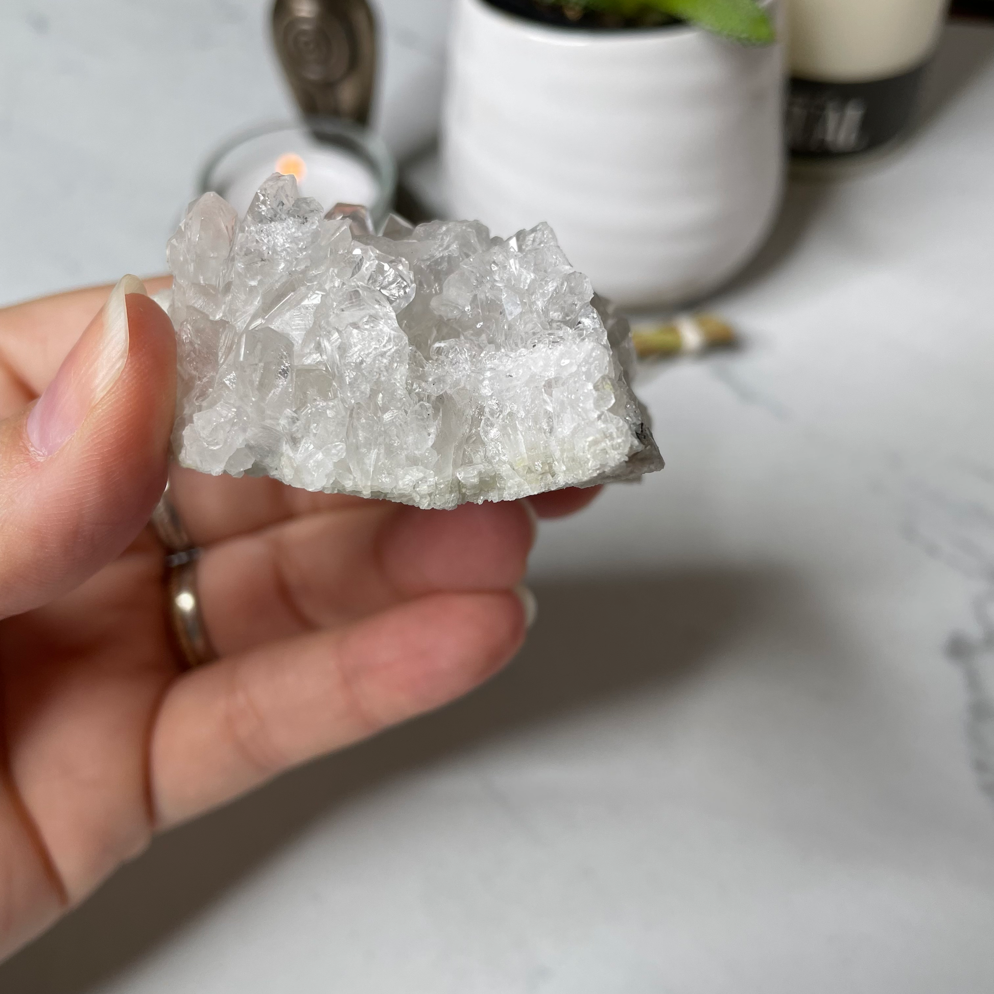 Freya's Haven | Metaphysical & Crystal shop | A close up photo of a Clear Quartz Cluster held in a woman's hand with candles in the background.