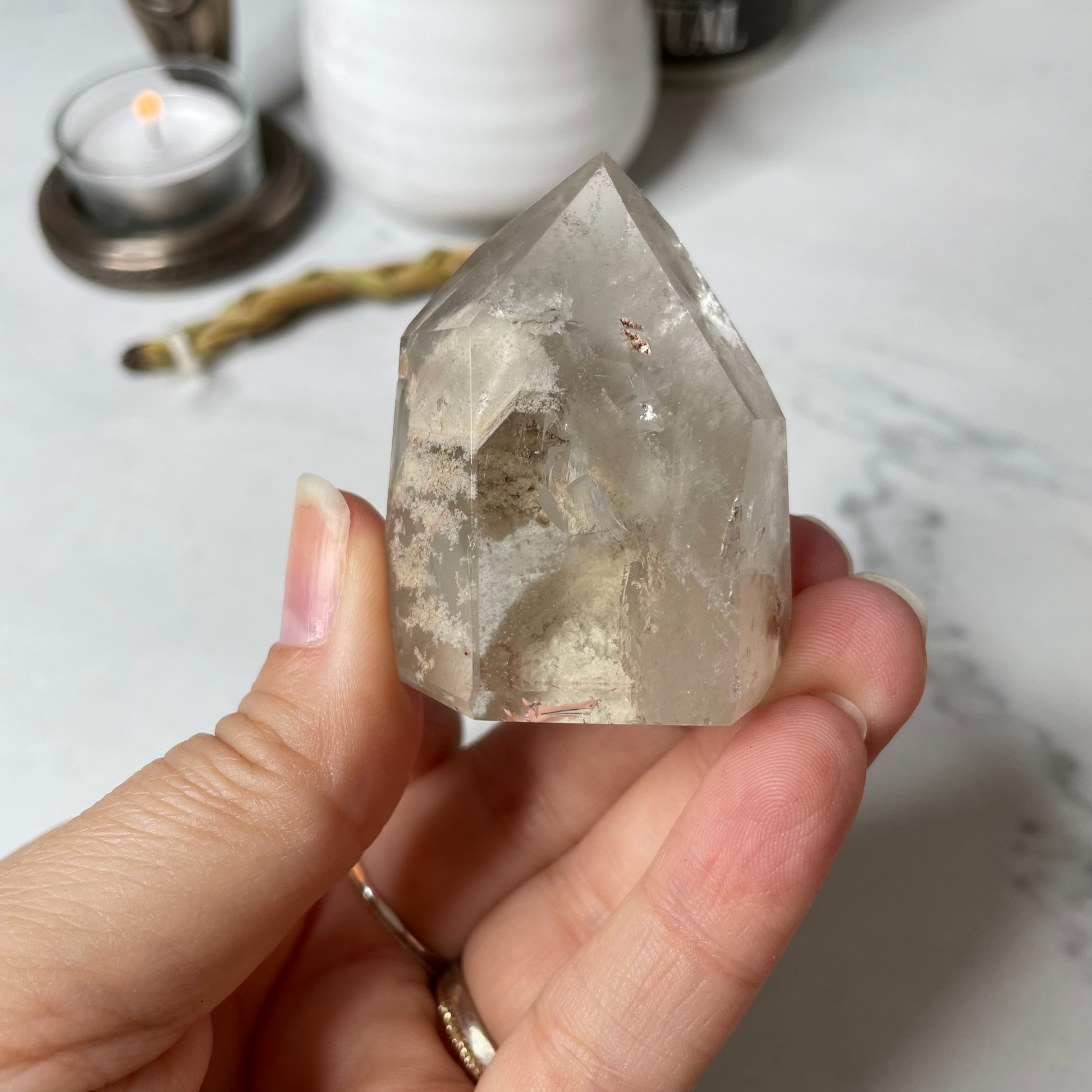 Freya's Haven | Metaphysical & Crystal shop | A close up photo of  a Lodalite  crystal held in a woman's hand with candles in the background.