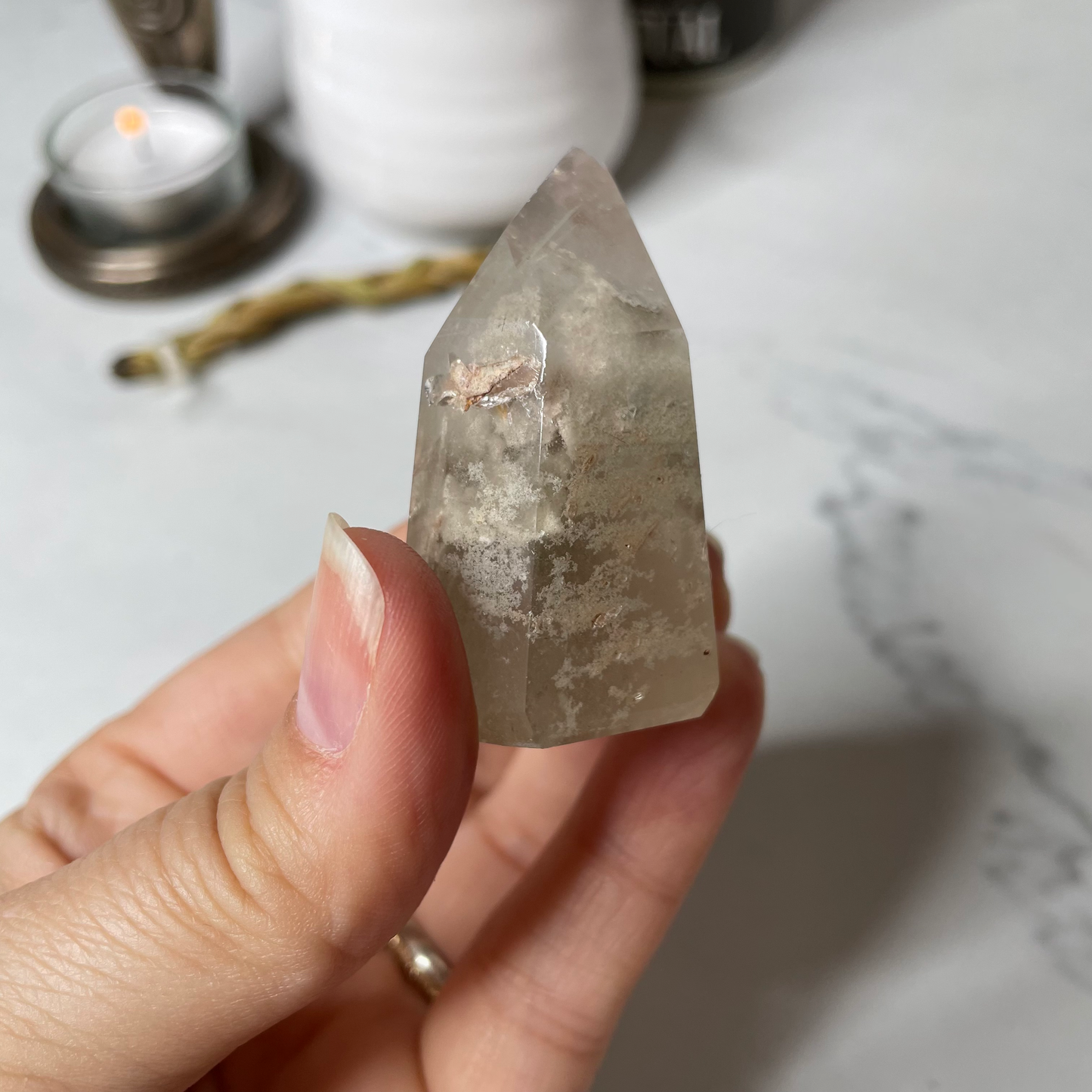 Freya's Haven | Metaphysical & Crystal shop | A close up photo of  a Lodalite  crystal held in a woman's hand with candles in the background.