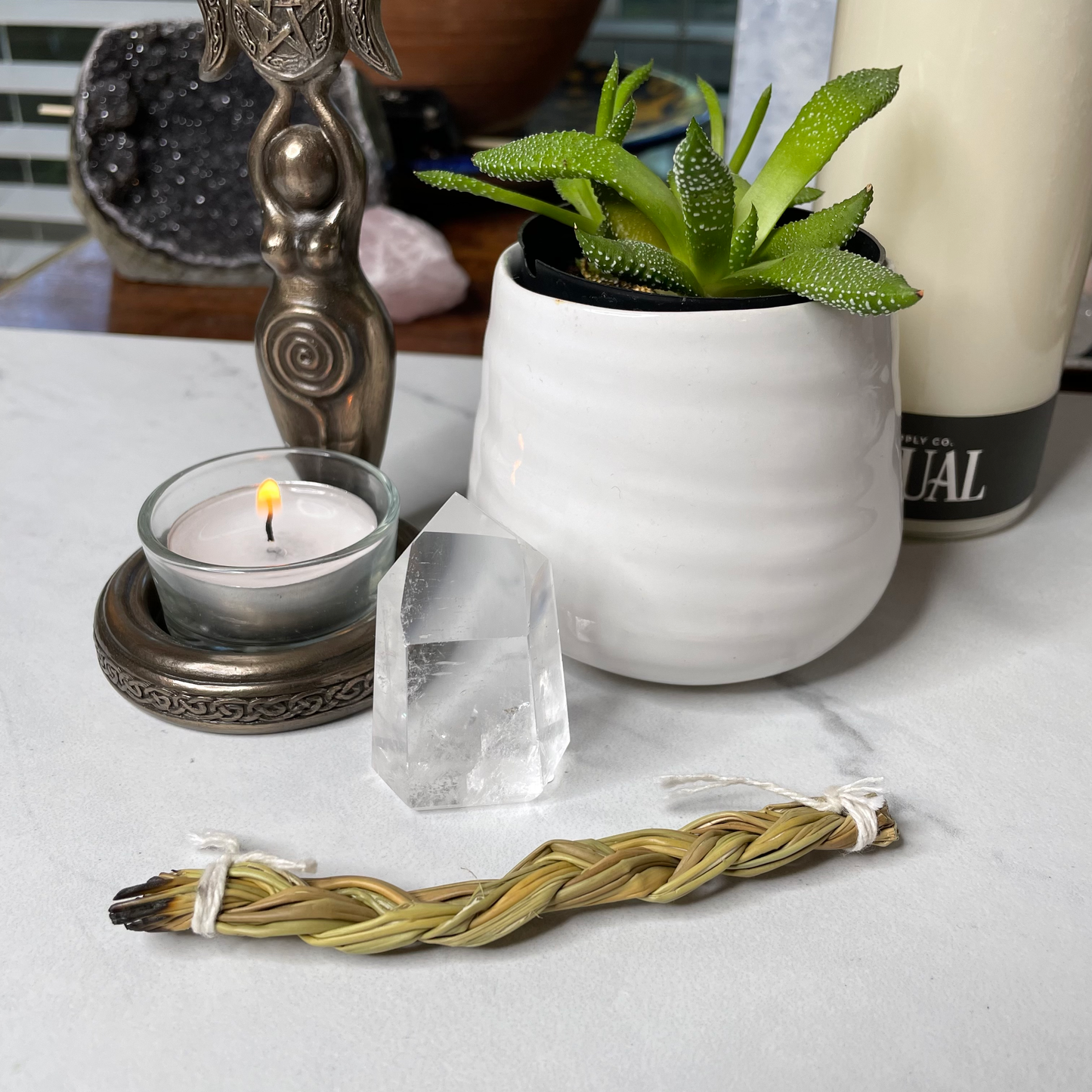 Freya's Haven | Metaphysical & Crystal shop | A Lemurian seed crystal is displayed with a succulent in a white pot, a goddess tea light candle holder with lit candle and a few books in the background.