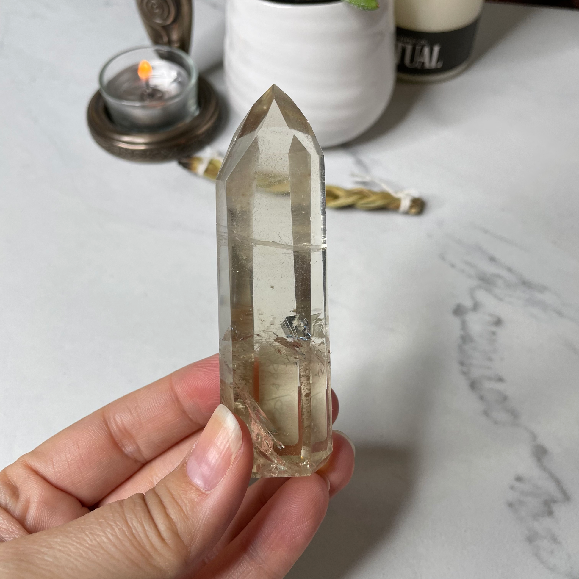 Freya's Haven | Metaphysical & Crystal shop | A close up photo of a Citrine Phantom tower held in a woman's hand with candles in the background.