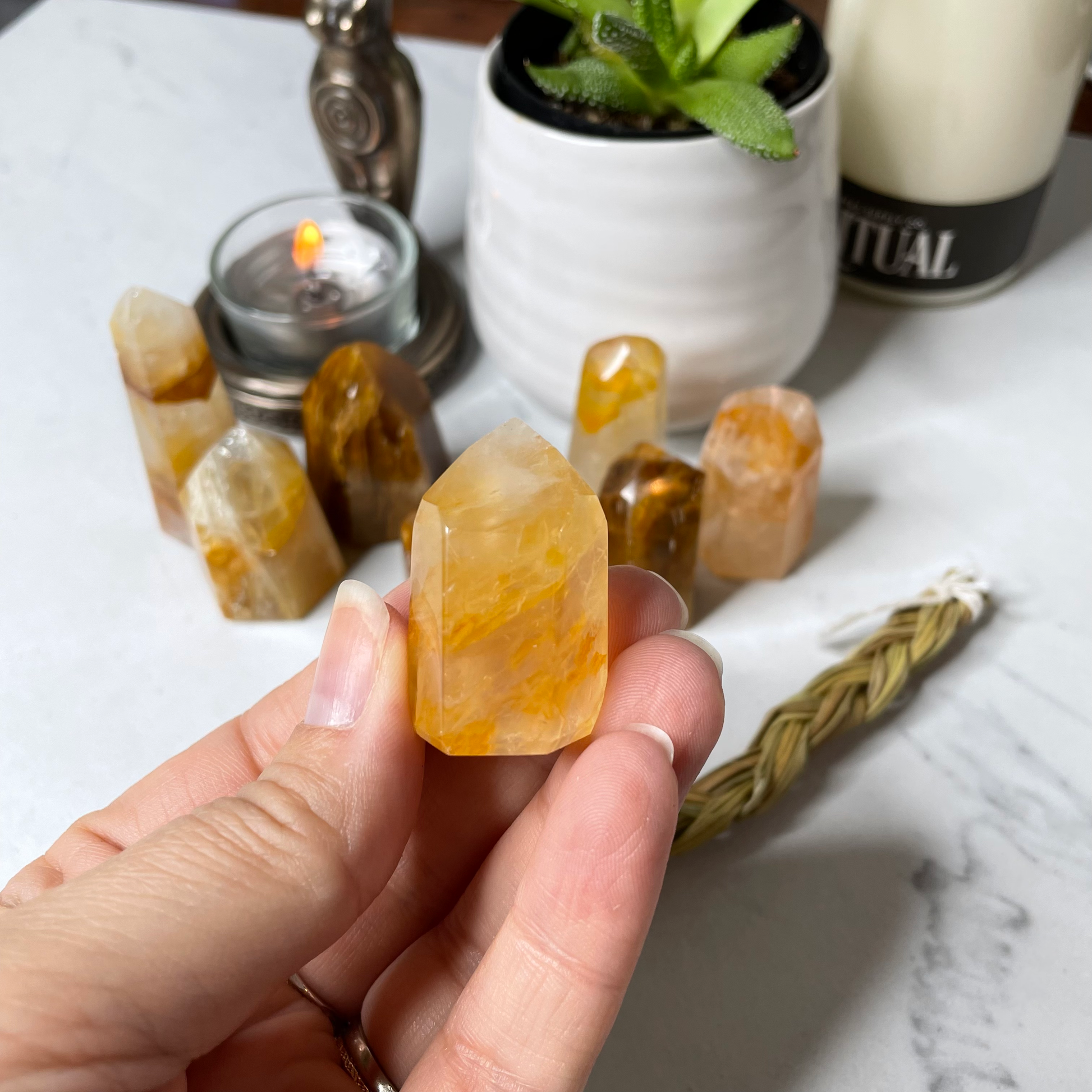 Freya's Haven | Metaphysical & Crystal shop | A close up photo of a Golden Healer tower held in a woman's hand with candles in the background.