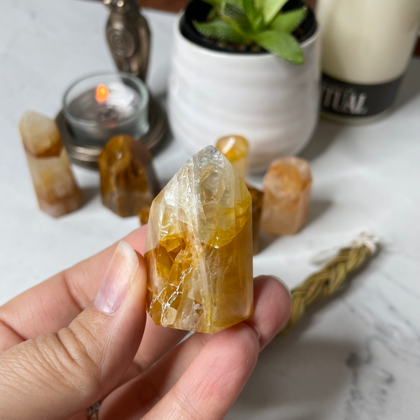 Freya's Haven | Metaphysical & Crystal shop | A close up photo of a Golden Healer tower held in a woman's hand with candles in the background.