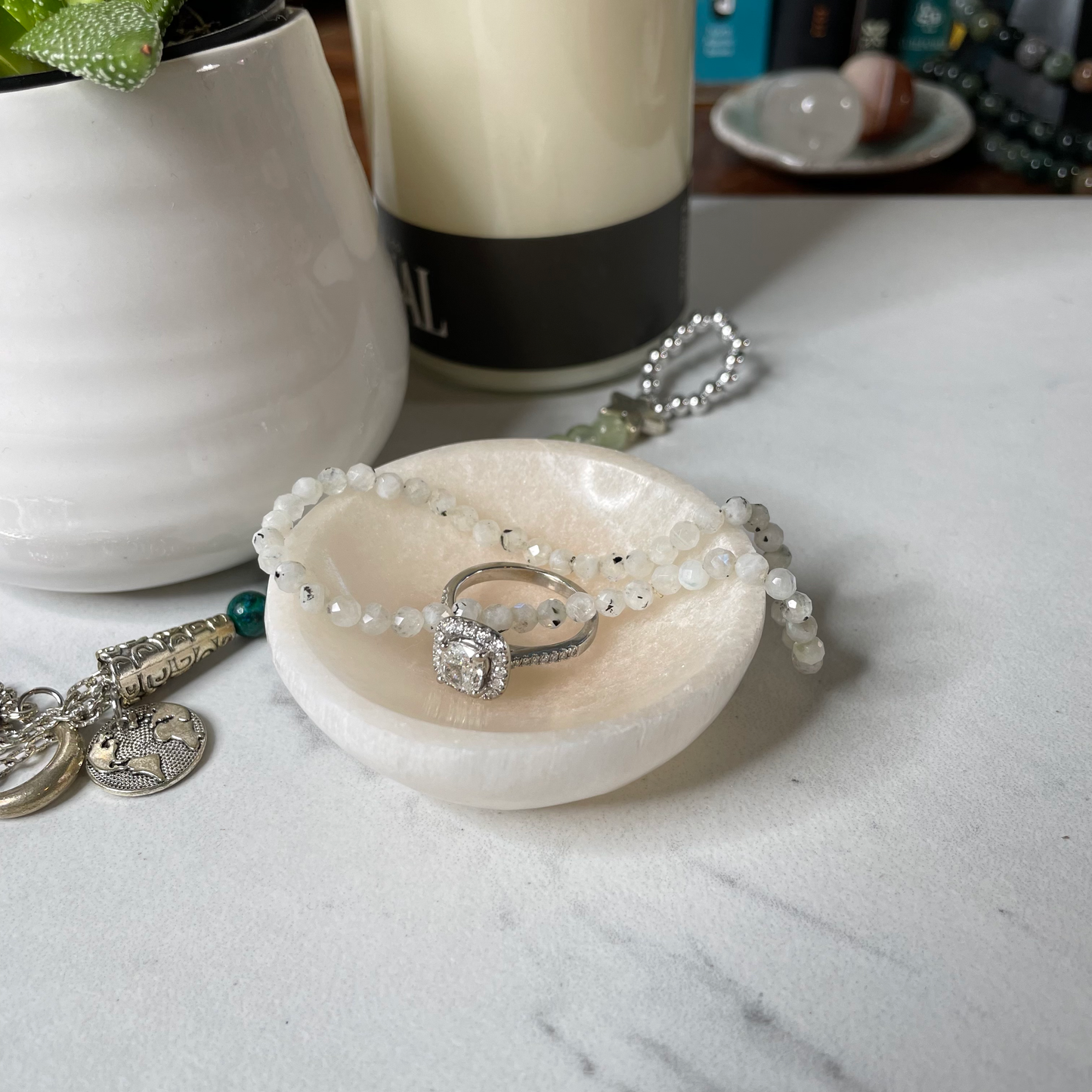 Freya's Haven | Metaphysical & Crystal shop | An orange Selenite bowl is displayed with a succulent in a white pot, a goddess tea light candle holder with lit candle with a bracelet and diamond engagement ring displayed inside the bowl.
