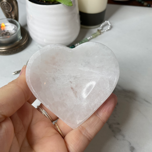 Freya's Haven | Metaphysical & Crystal shop | A close up photo of  a heart-shaped Selenite bowl held in a woman's hand with candles in the background.