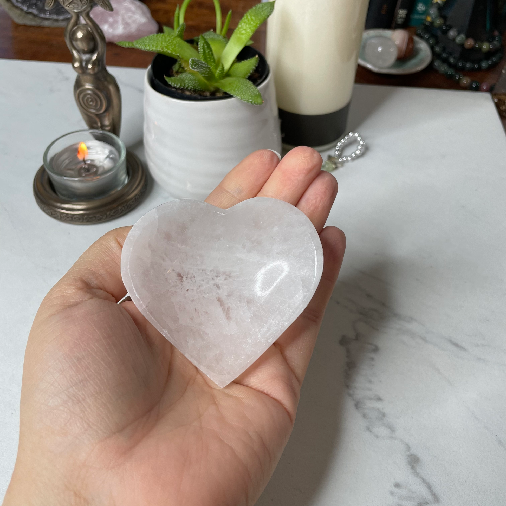 Freya's Haven | Metaphysical & Crystal shop | A close up photo of  a heart-shaped Selenite bowl held in a woman's hand with candles in the background.