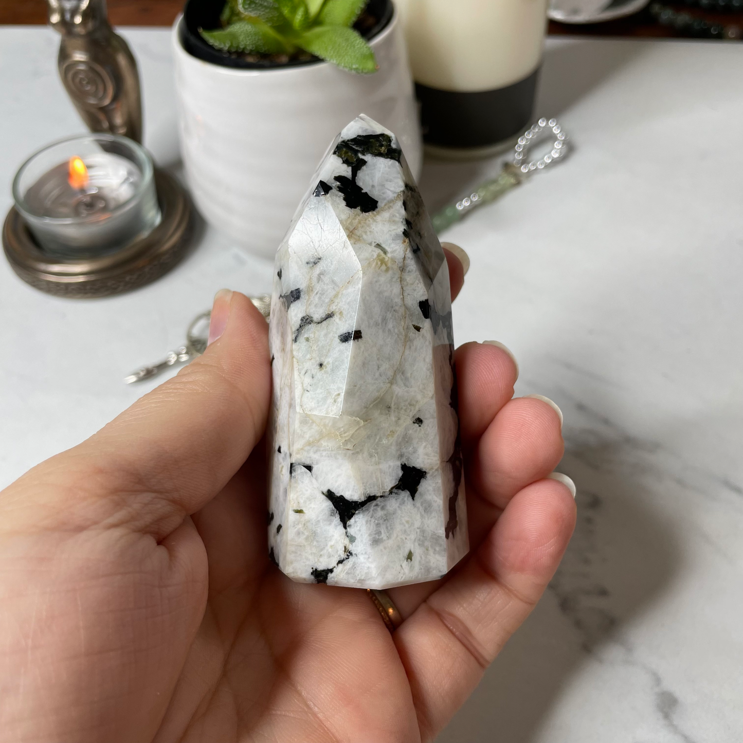 Freya's Haven | Metaphysical & Crystal shop | A close up photo of  a Rainbow Moonstone tower held in a woman's hand with candles in the background.