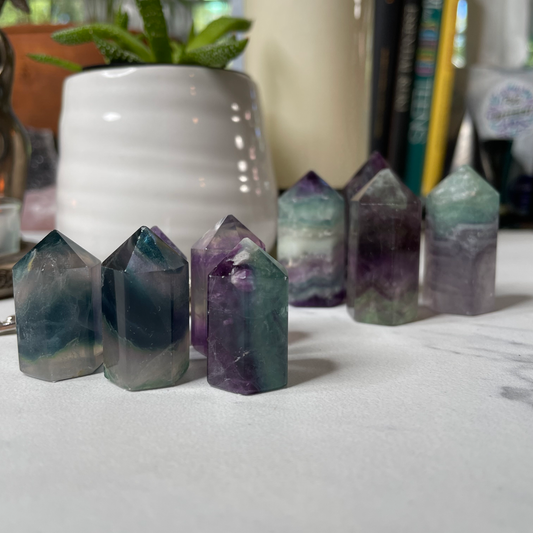 Freya's Haven | Metaphysical & Crystal shop | A group of Rainbow Fluorite  towers are displayed with a succulent in a white pot, a goddess tea light candle holder with lit candle and a few books in the background.