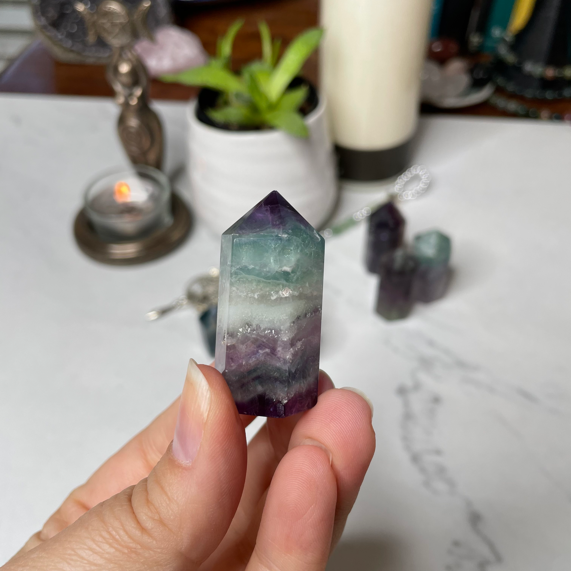 Freya's Haven | Metaphysical & Crystal shop | A close up photo of  a Rainbow Fluorite tower held in a woman's hand with candles in the background.