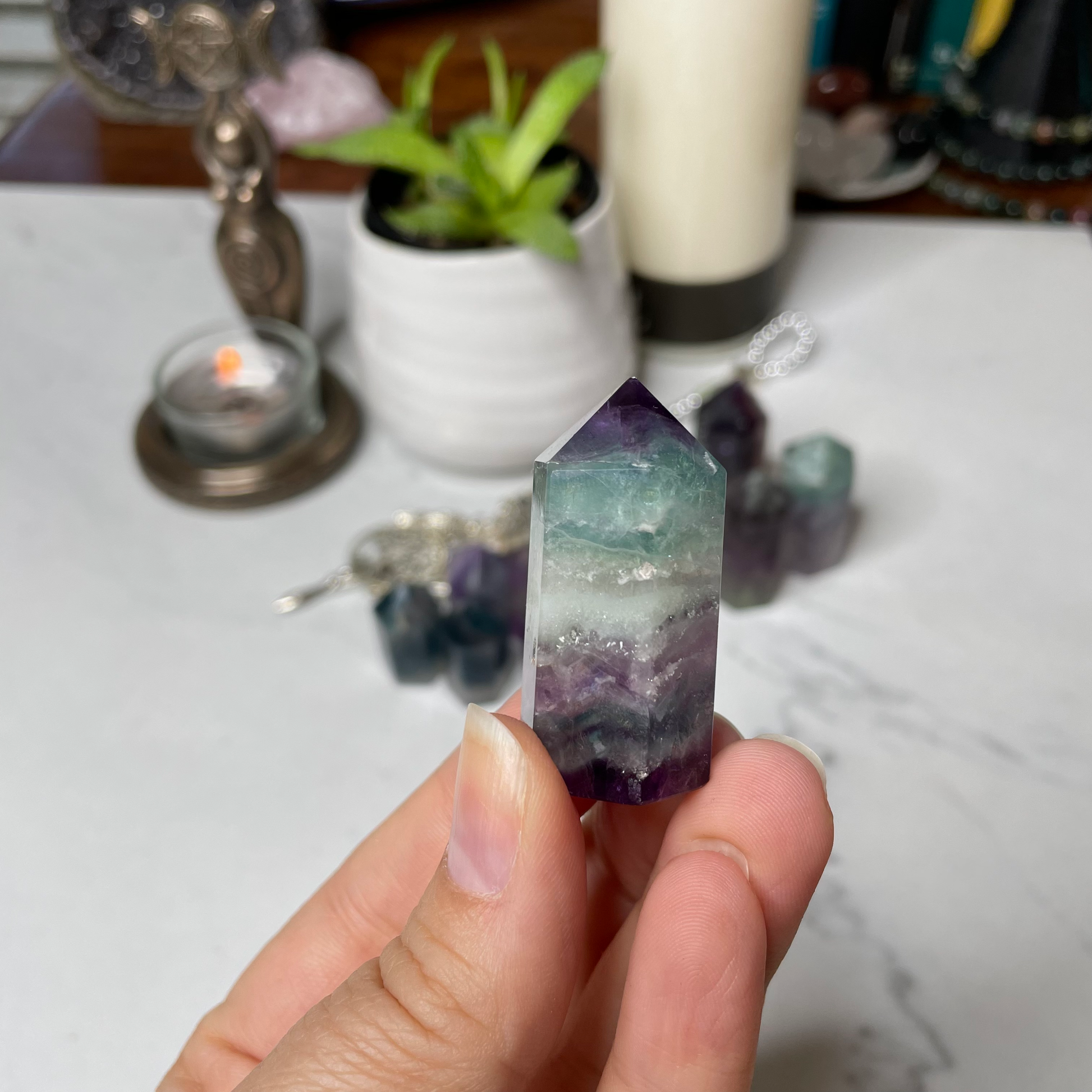 Freya's Haven | Metaphysical & Crystal shop | A close up photo of  a Rainbow Fluorite tower held in a woman's hand with candles in the background.