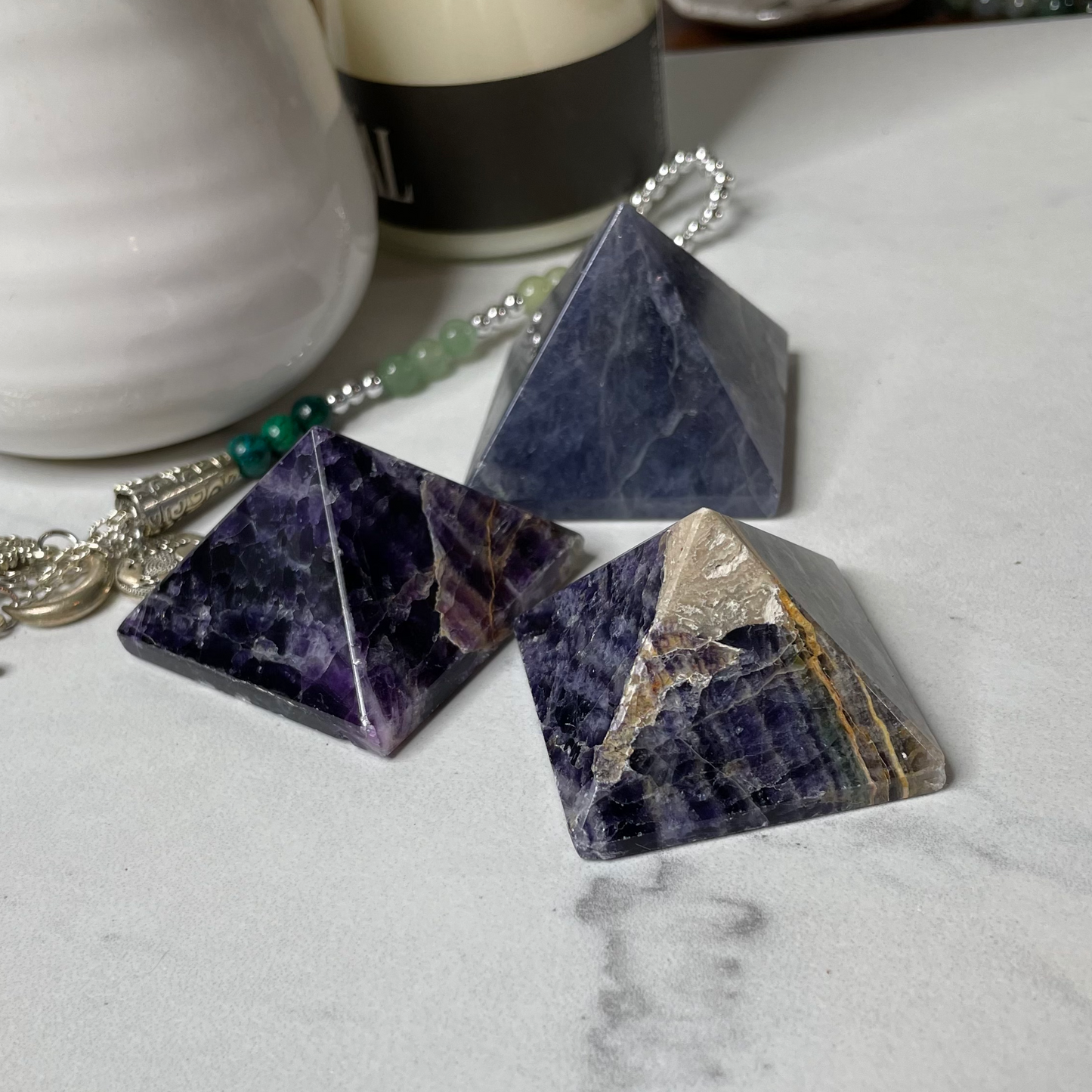 Freya's Haven | Metaphysical & Crystal shop | A group of Rainbow Fluorite  pyramids are displayed with a succulent in a white pot, a goddess tea light candle holder with lit candle and a few books in the background.