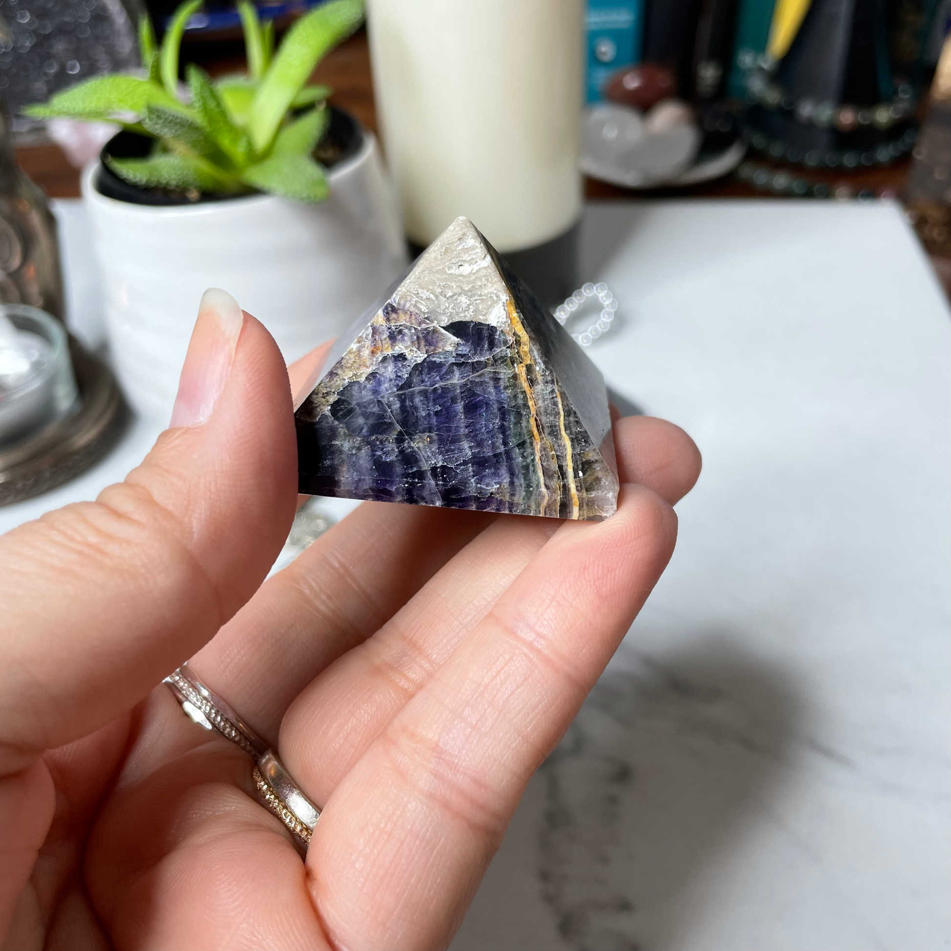 Freya's Haven | Metaphysical & Crystal shop | A close up photo of  a Rainbow Fluorite pyramid held in a woman's hand with candles in the background.