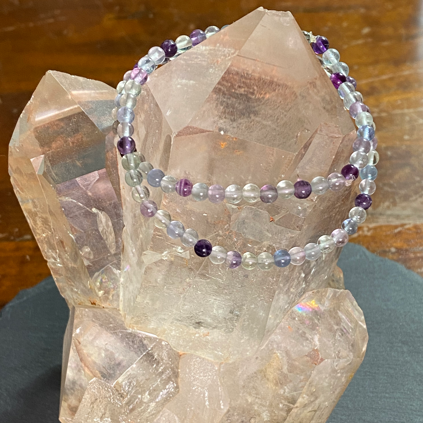 Two rainbow fluorite bracelets are displayed on a quartz point cluster.