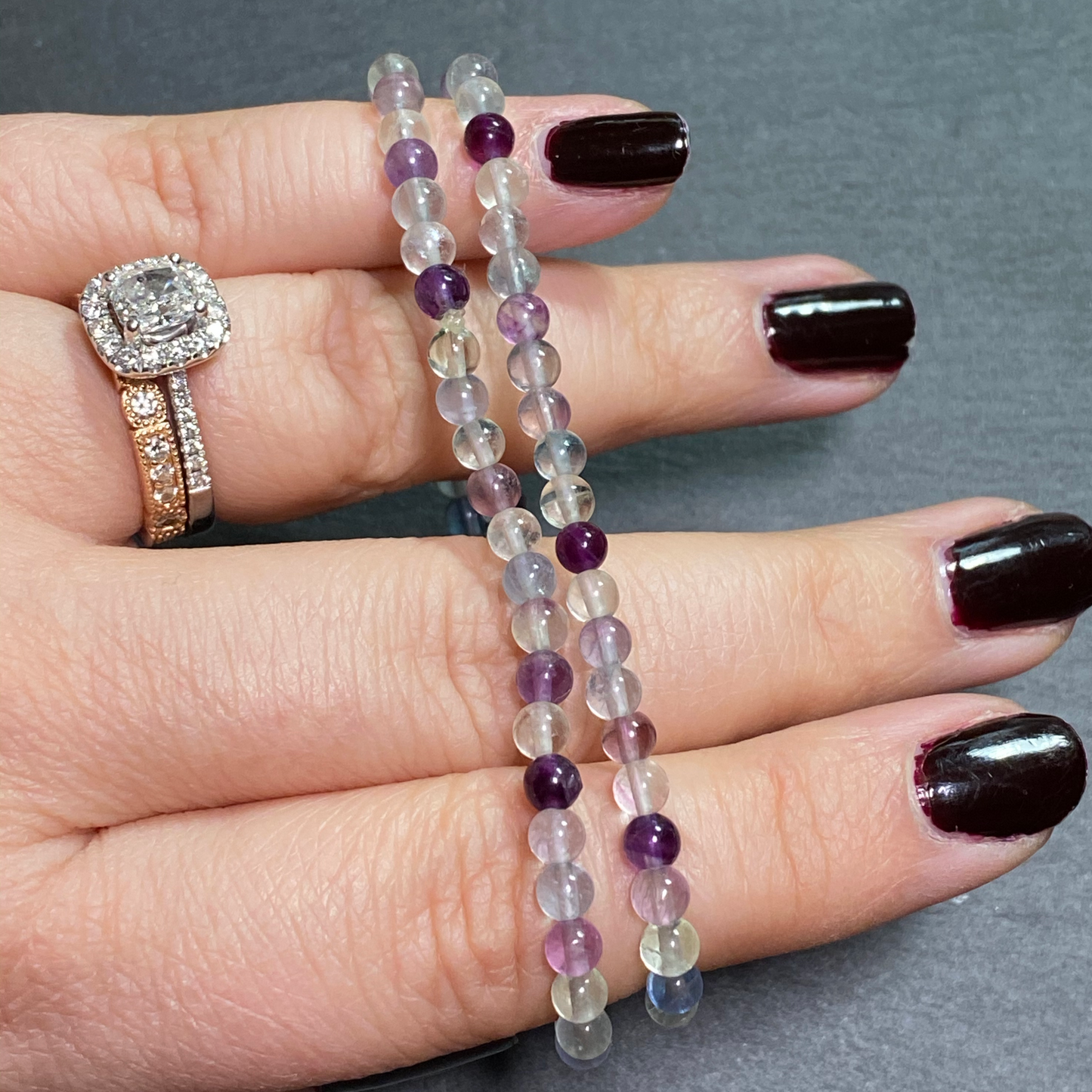Two rainbow fluorite bracelets are displayed across a woman's fingers.