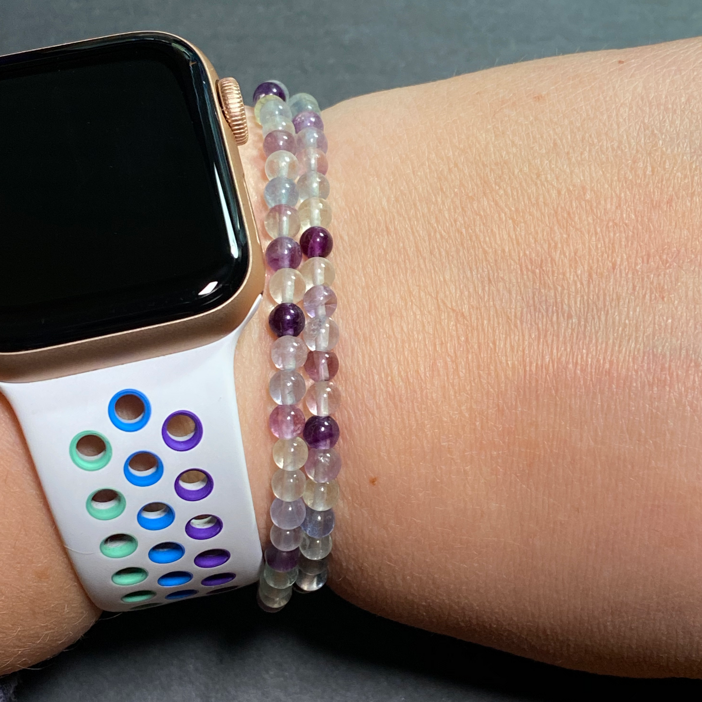 Two rainbow fluorite bracelets are displayed on a woman's wrist next to an Apple watch.