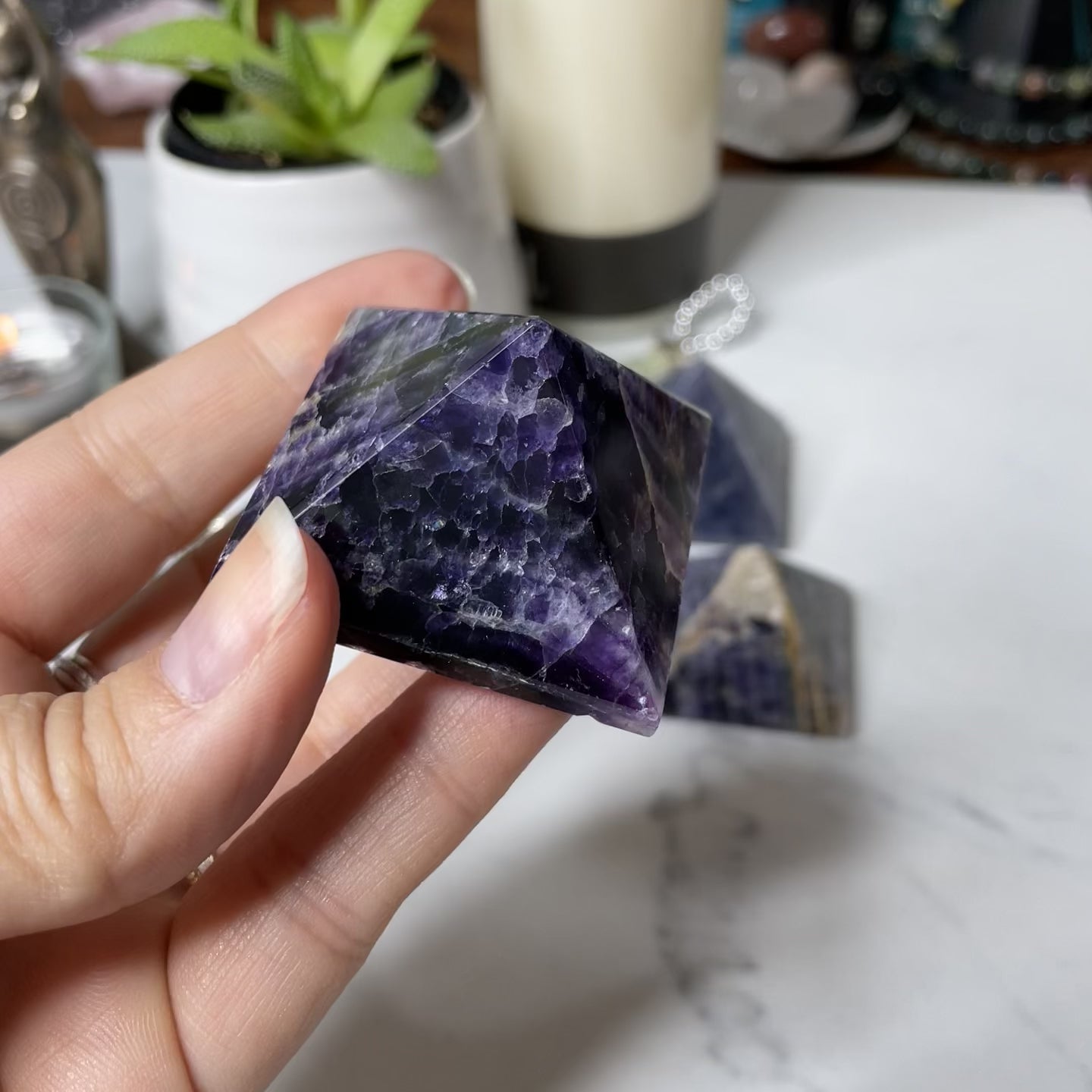 Freya's Haven | Metaphysical & Crystal shop | A close up video of a Rainbow Fluorite pyramid held in a woman's hand with candles in the background.