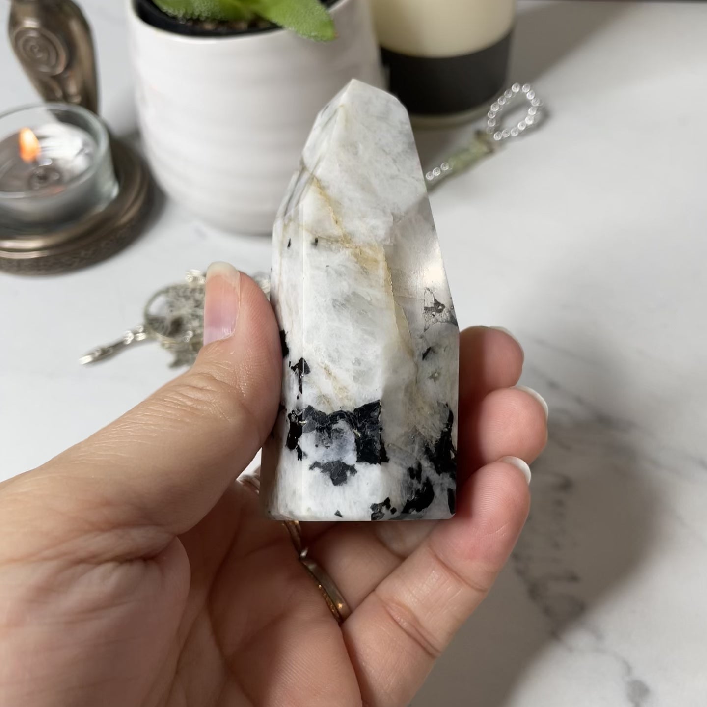 Freya's Haven | Metaphysical & Crystal shop | A close up video of a Rainbow Moonstone tower held in a woman's hand with candles in the background.